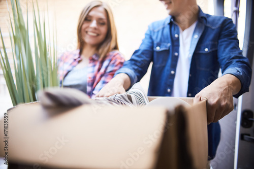 Portrait of smiling man and woman putting cardboard box into moving van