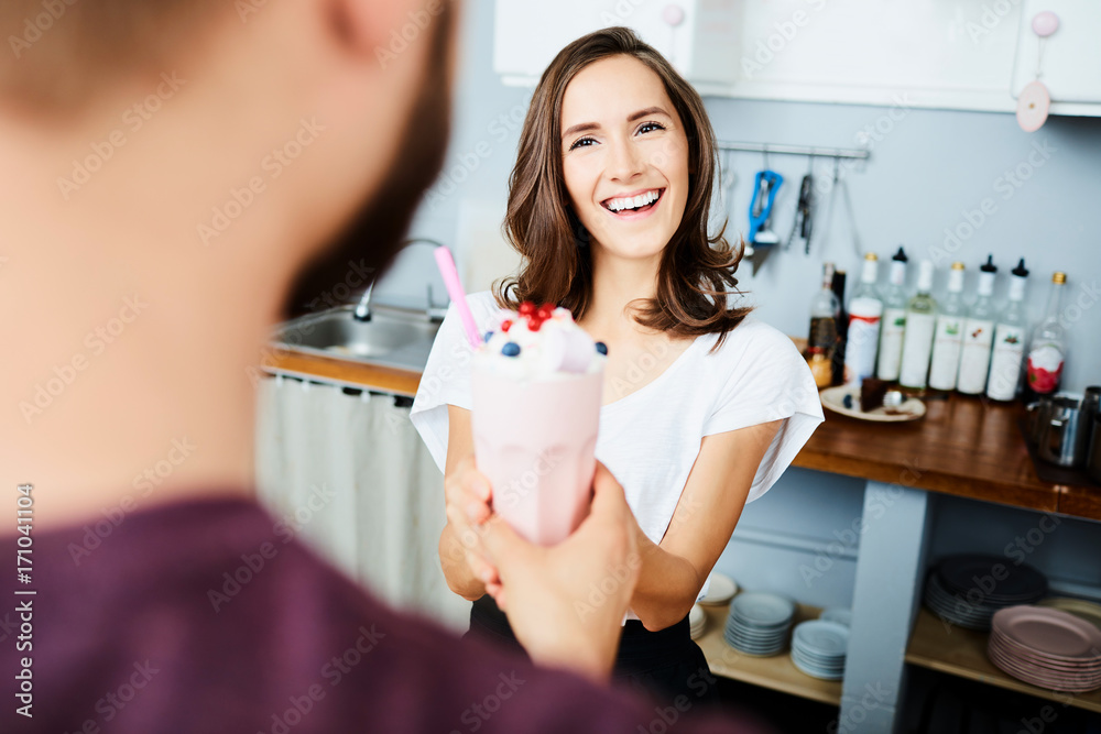 smiling woman giving milkshake to customer in stylish modern cafe smiling woman giving milkshake to customer in stylish modern cafe