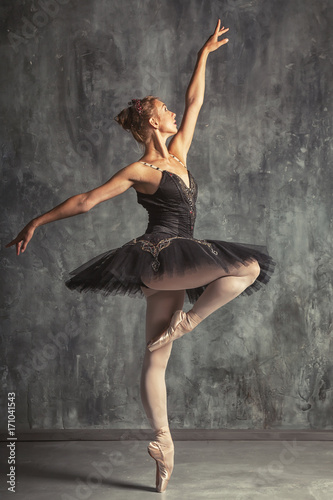 Young beautiful woman prima theater in a black festive pack, white pantyhose, white pointe shoes beautifully dancing russian ballet in a black dance studio