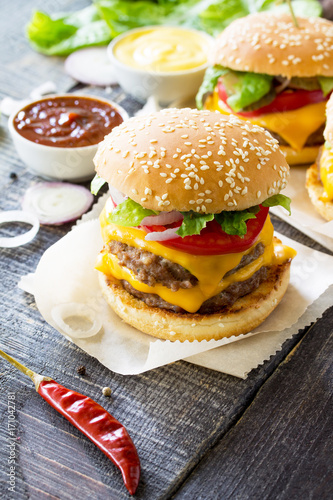 Delicious fresh homemade double cheeseburger on a wooden kitchen table. Double burger with meat cutlet and vegetables. Street food, fast food.