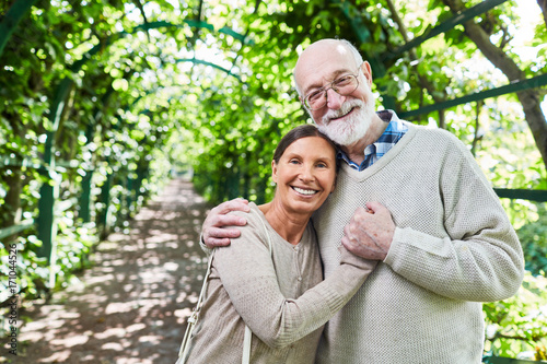 Aged couple standing in embrace in green alleyway in natural environment © pressmaster