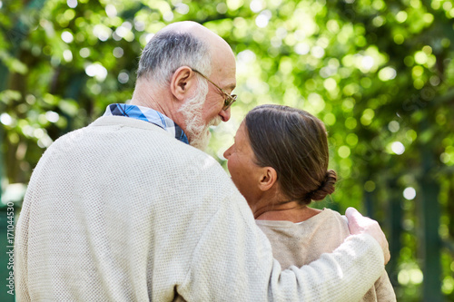 Back view of happy amorous seniors spending time in summer park