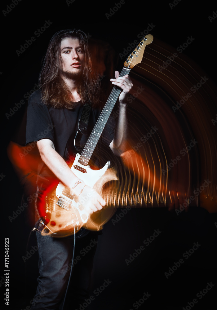 Studio portrait: handsome young long-haired man (rock musician) playing the electric guitar. Blurry (motion) effect