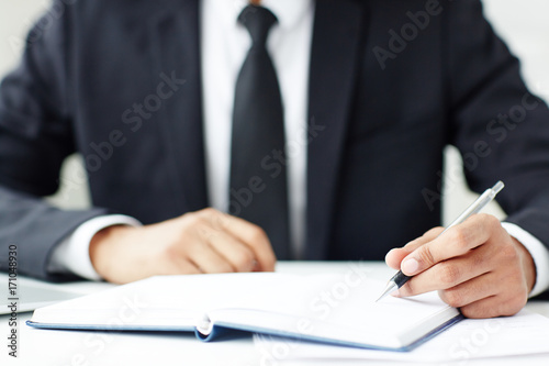 Manager in formalwear writing down agenda points in notebook