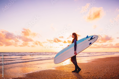 Surf girl holding surfboard at sunset or sunrise and ocean.