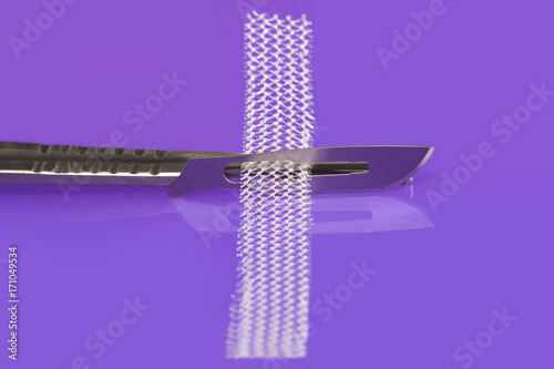 Surgical knife and tension-free vaginal tape for TVT operation on lilac background photo