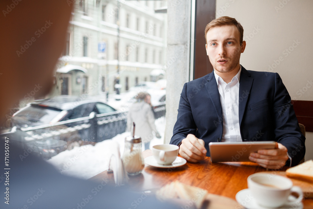 Financial expert with touchpad communicating with client or co-worker at meeting Financial expert with touchpad communicating with client or co-worker at meeting