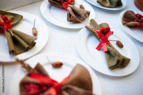 Several plates with napkins decorated by red ribbons, wheat spikes and ripe ashberries photo