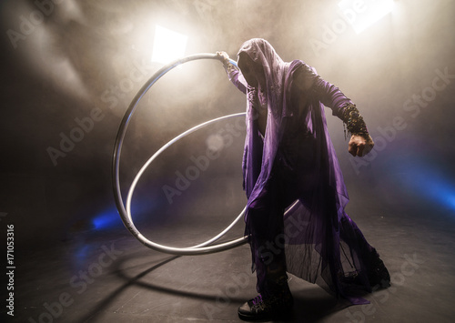 Fairy-tale character assassin in a purple cloak with a hood with two large cyr wheel hoops