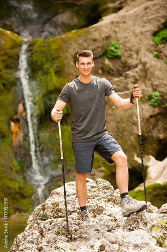 Active young man hiking in mountains near waterfall on a creek