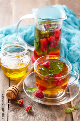 Glass cup of hot tea with raspberries, mint and honey