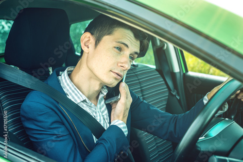 Man driver talking on a phone in the car. Distracted and dangerous driving. The traffic violation. © Artem