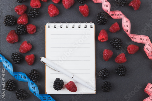 Red raspberries, tape measure, notebook and a pen on the black slate stone background photo