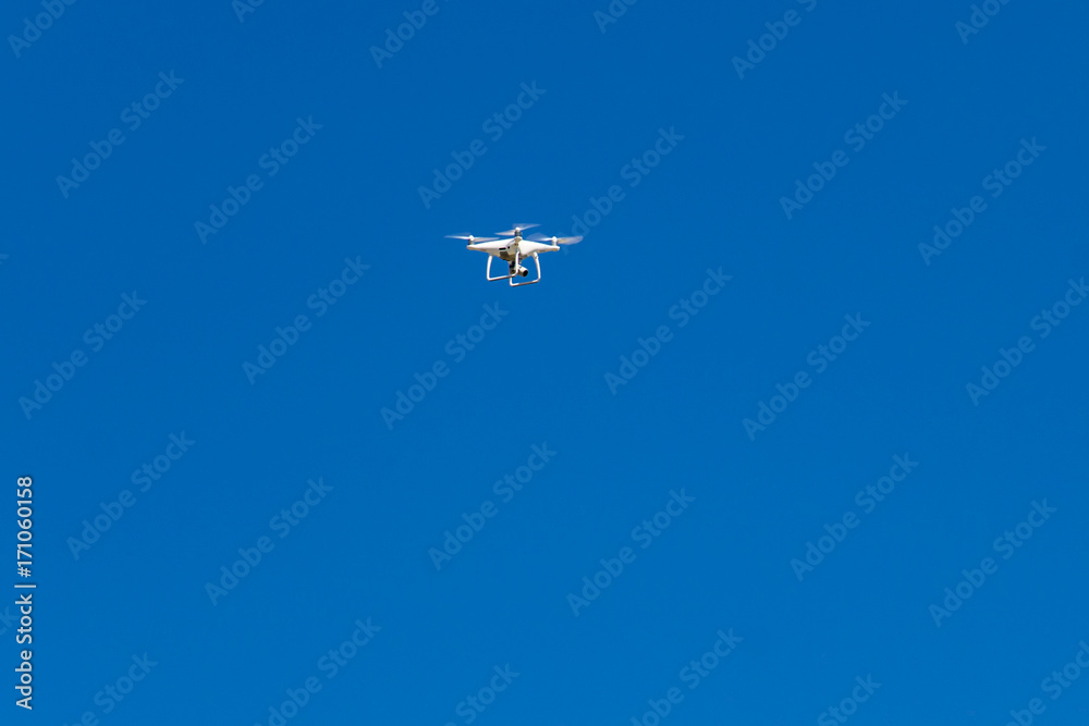Quadcopter drone with the camera hovering in blue sky