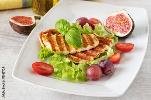 Grilled slices of halloumi cheese served on the plate with fig  grapes  lettuce  tomatoes and basil leaf. Halloumi is popular in Cyprus  Greece  and Turkey.