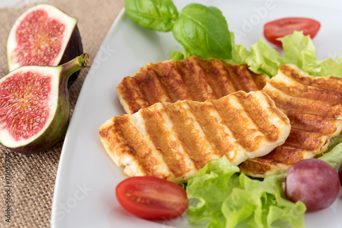 Grilled slices of halloumi cheese served on the plate with fig, grapes, lettuce, tomatoes and basil leaf. Halloumi is popular in Cyprus, Greece, and Turkey.
