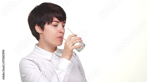 confident caucasian lady looking at camera and drinking water from glass isolated over white background in slowmotion photo