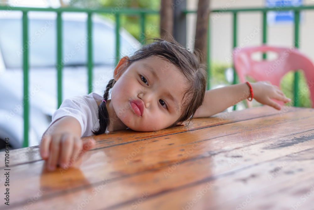 Adorable cute asian baby girl in white t-shirt making pig mouth and put her face on wooden table.