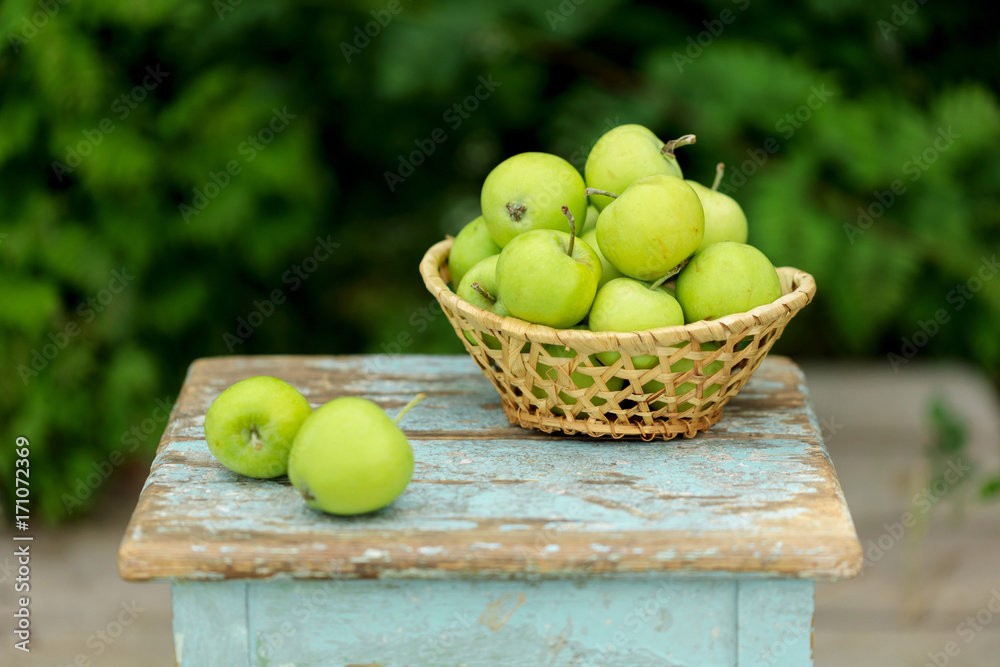 Homemade rustic green apples in a basket on an old stool. Homemade rustic green apples in a basket on an old stool.