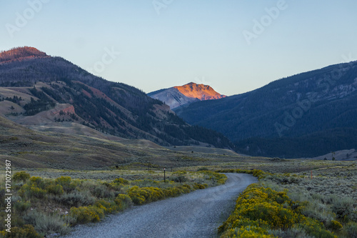 dirt road winding through a mountain valley towards a peak at sunset