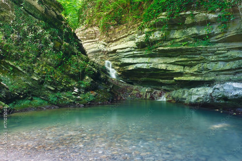 Naklejka premium Forested rocks covered with ivy and moss with a waterfall flowing down