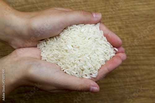Female hands full of white rice on wooden background