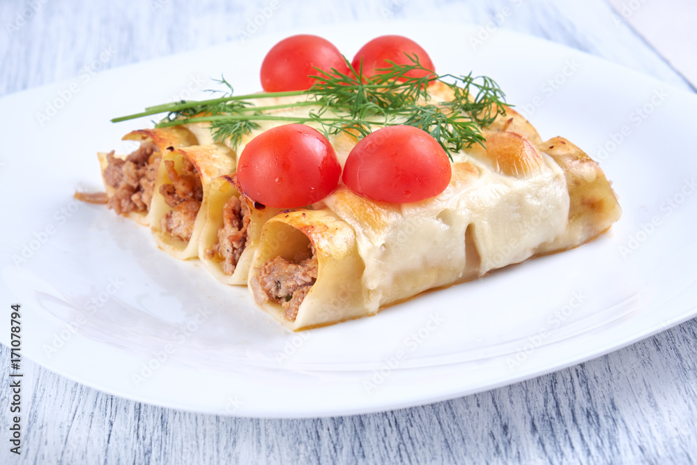 Baked cannelloni with cheese and tomatoes on a white plate Baked cannelloni with cheese and tomatoes on a white plate