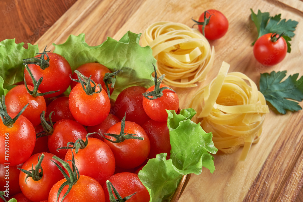 Tomatoes in a wicker basket and green leaves of salad, pasta nests on a wooden Board Tomatoes in a wicker basket and green leaves of salad, pasta nests on a wooden Board