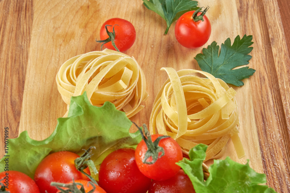 Tomatoes in a wicker basket and green leaves of salad, pasta nests on a wooden Board Tomatoes in a wicker basket and green leaves of salad, pasta nests on a wooden Board