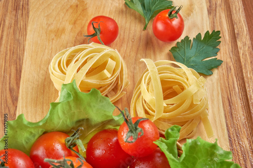Tomatoes in a wicker basket and green leaves of salad, pasta nests on a wooden Board