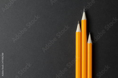 Three yellow pencils on black paper, empty space.