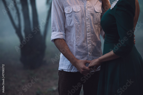 Loving couple in a foggy forest, they hold hands