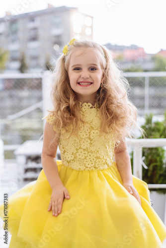 Portrait of a beautiful smiling little girl in a yellow dress with long blond hair