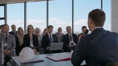 Business speaker standing behind tribune and talking in micrphone in front of audience