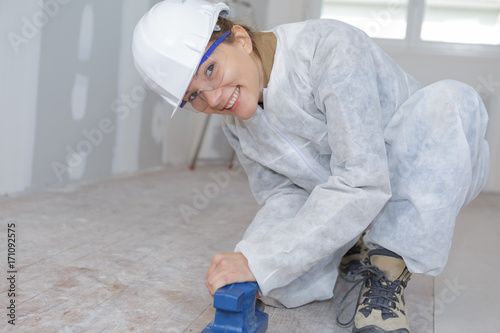 happy female contractor sanding wooden floor in workshop