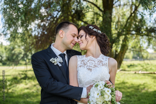 likable and pretty wedding couple stay and hugging and kissing in the garden by the tree