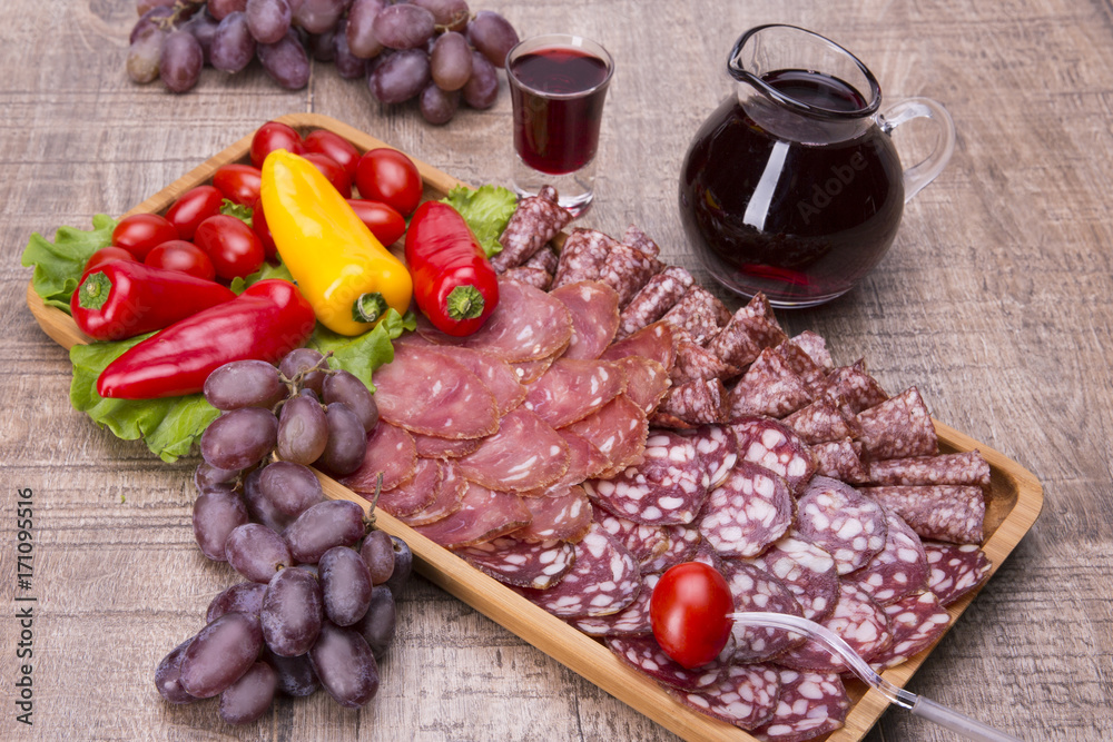 Set of meat delicatessen, tomatoes and peppers, wine on a wooden table.