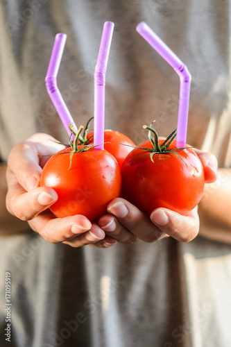 Three Ripe Red Tomatoes with Straws in Woman Hands on Bright Background. Fresh Juice Healthy Food Concept. Tomato as a Vessel with Fresh Juice photo