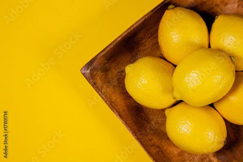 Fresh lemons on a wooden plate from above on a yellow background