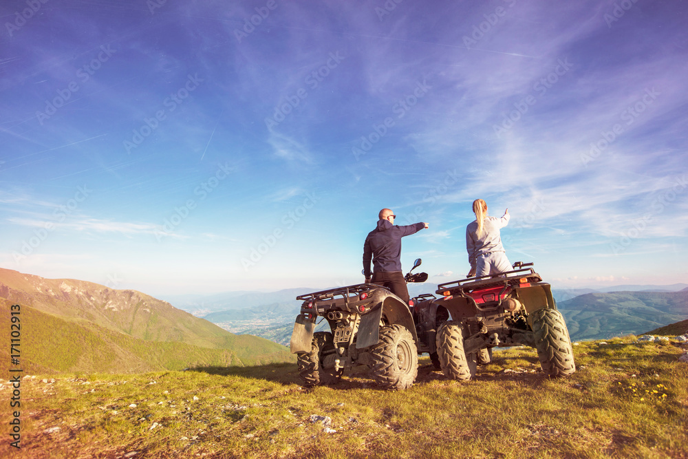 Obraz premium Rear view of young pair near atv. Man is showing something in distance to her girlfriend.