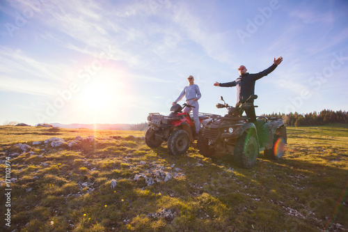 Rear view of young pair near atv. Man is showing something in distance to her girlfriend.