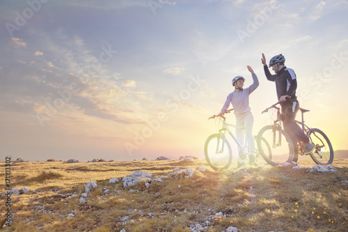 happy couple goes on a mountain asphalt road in the woods on bikes with helmets giving each other a high five