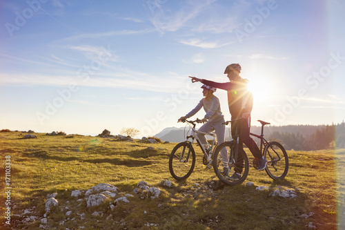 Biker couple with mountain bike pointing in distance at countryside © FS-Stock