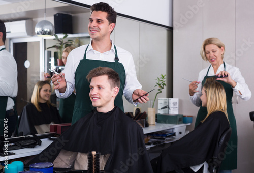 Positive male hairstyler serving teenager in chair