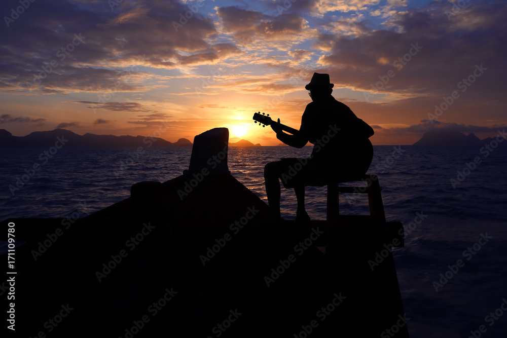 Silhouette man playing a guitar on the boat with blue sky sunrise