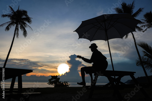 Man playing guitar on the beach with blue sky sunrise