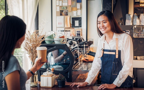 Asian woman barista wear jean apron served to go coffee cup  to customer at bar counter with smile emotion,Cafe restaurant service concept,Owner small business concept