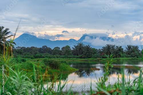 Evening scenic view of mountains behind lake and jungle with grass in foreground from Nakhon Si Thammarat province, south of thailand.