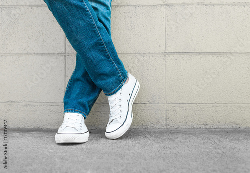 Young person posing in blue jeans and sneakers against brick wall. Fashion, youth concept.