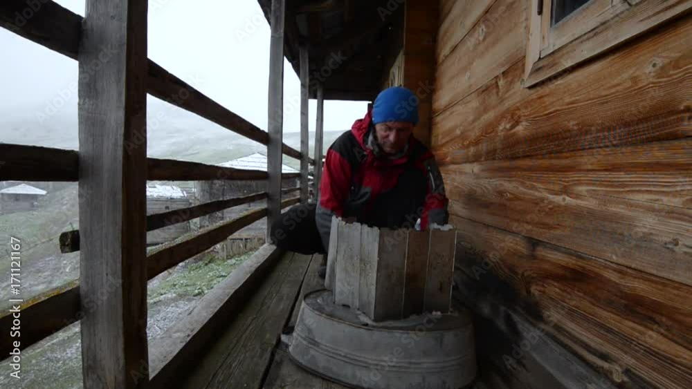 Adventurer man is cooking food on a small gas stove on the veranda of a abandoned wooden hut during a snowfall in the mountains. Epic travel in a mountains of Georgia. Adventurer man is cooking food on a small gas stove on the veranda of a abandoned wooden hut during a snowfall in the mountains. Epic travel in a mountains of Georgia.